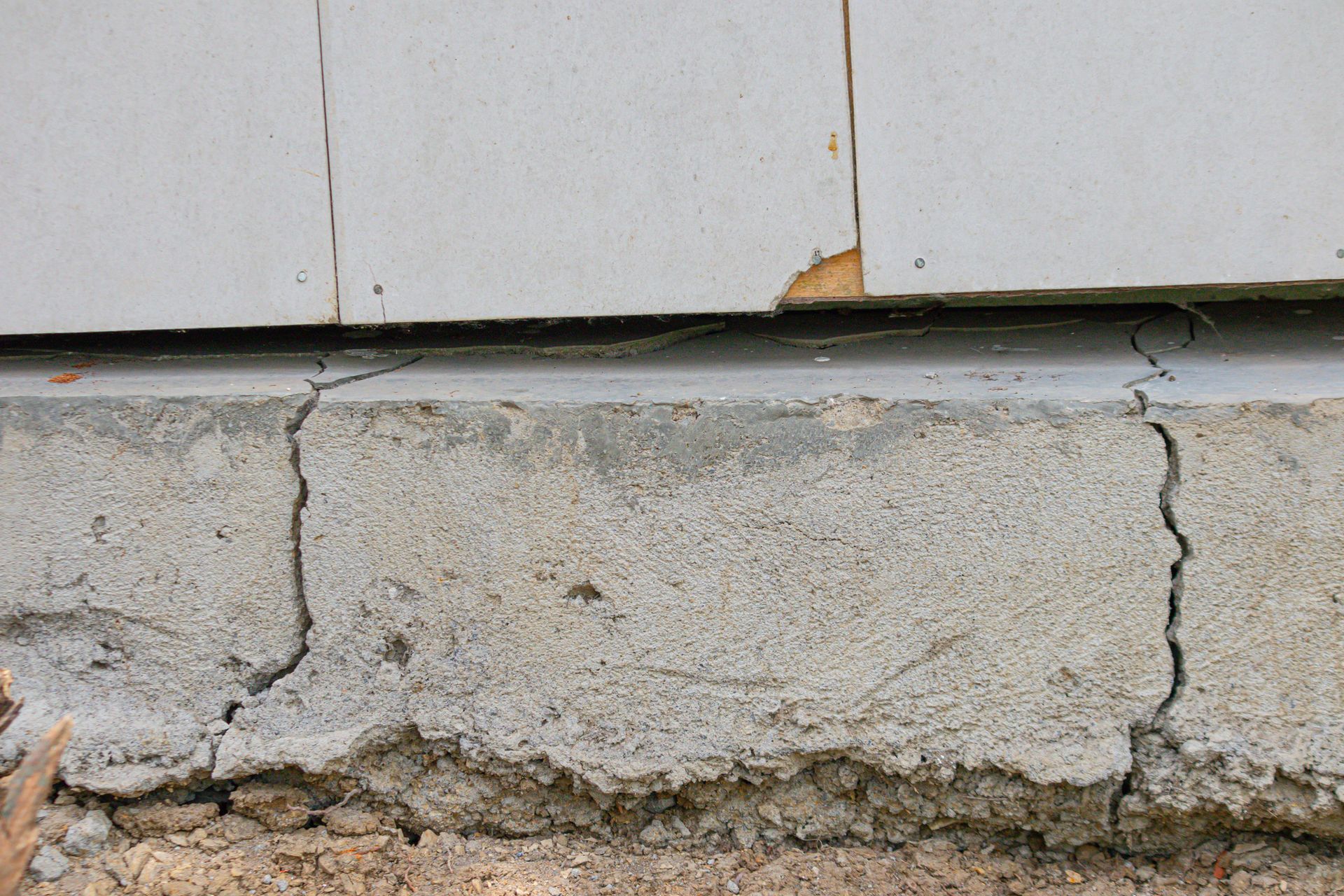 Cracked concrete foundation beneath white siding with a vertical split and chipped edge