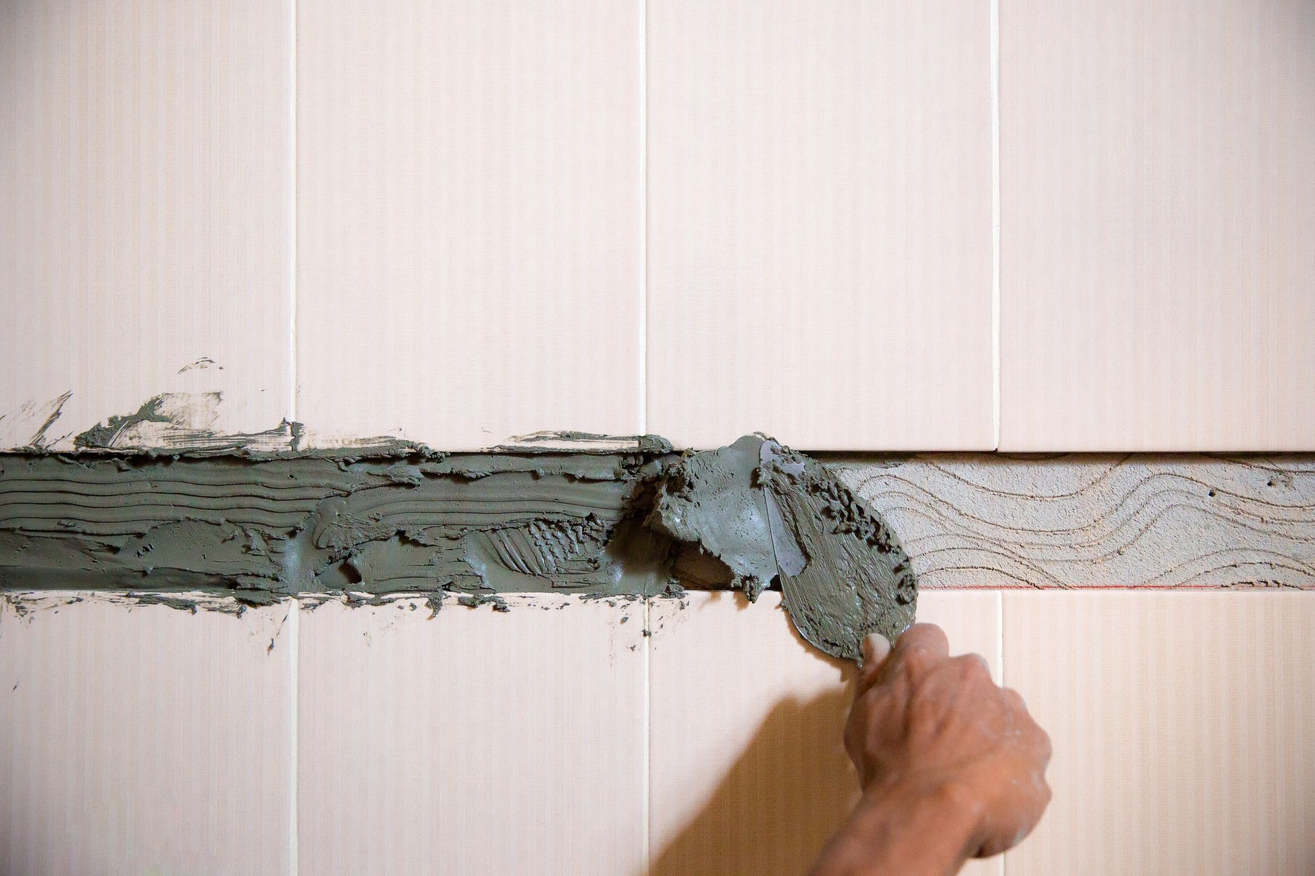 A hand spreads gray mortar over a horizontal crack in a white wall.