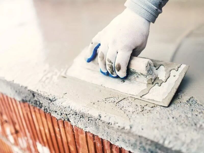 Gloved hand spreading wet concrete over a brick surface with a trowel Gloved hand spreading wet concrete over a brick surface with a trowel