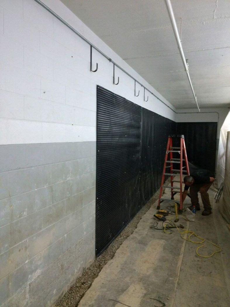 Worker on a red ladder installing a black wall panel in a narrow hallway.