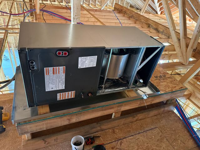 Black HVAC unit on a wooden platform inside an unfinished attic with exposed rafters