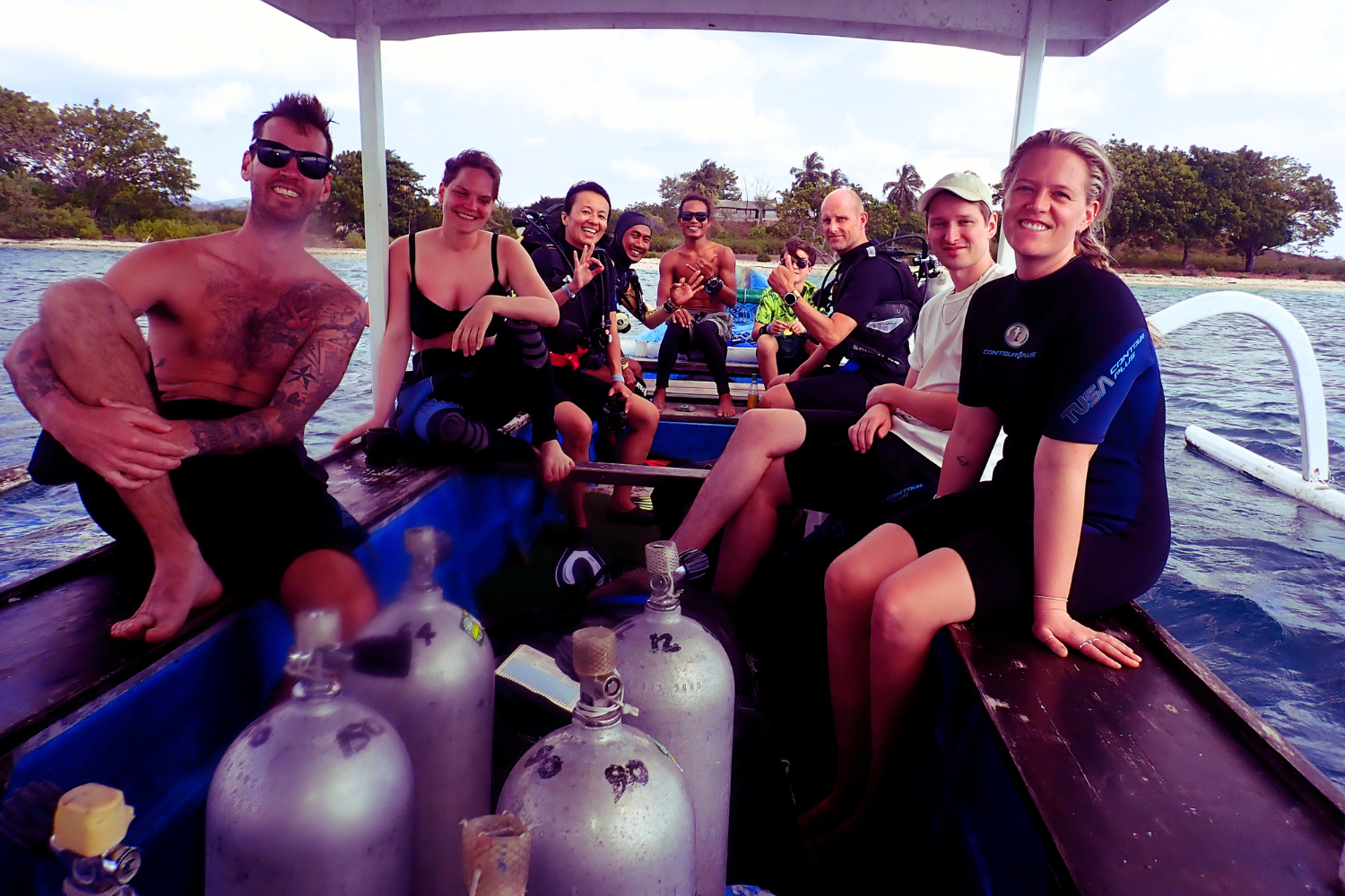 A group of people are sitting on a boat with scuba tanks