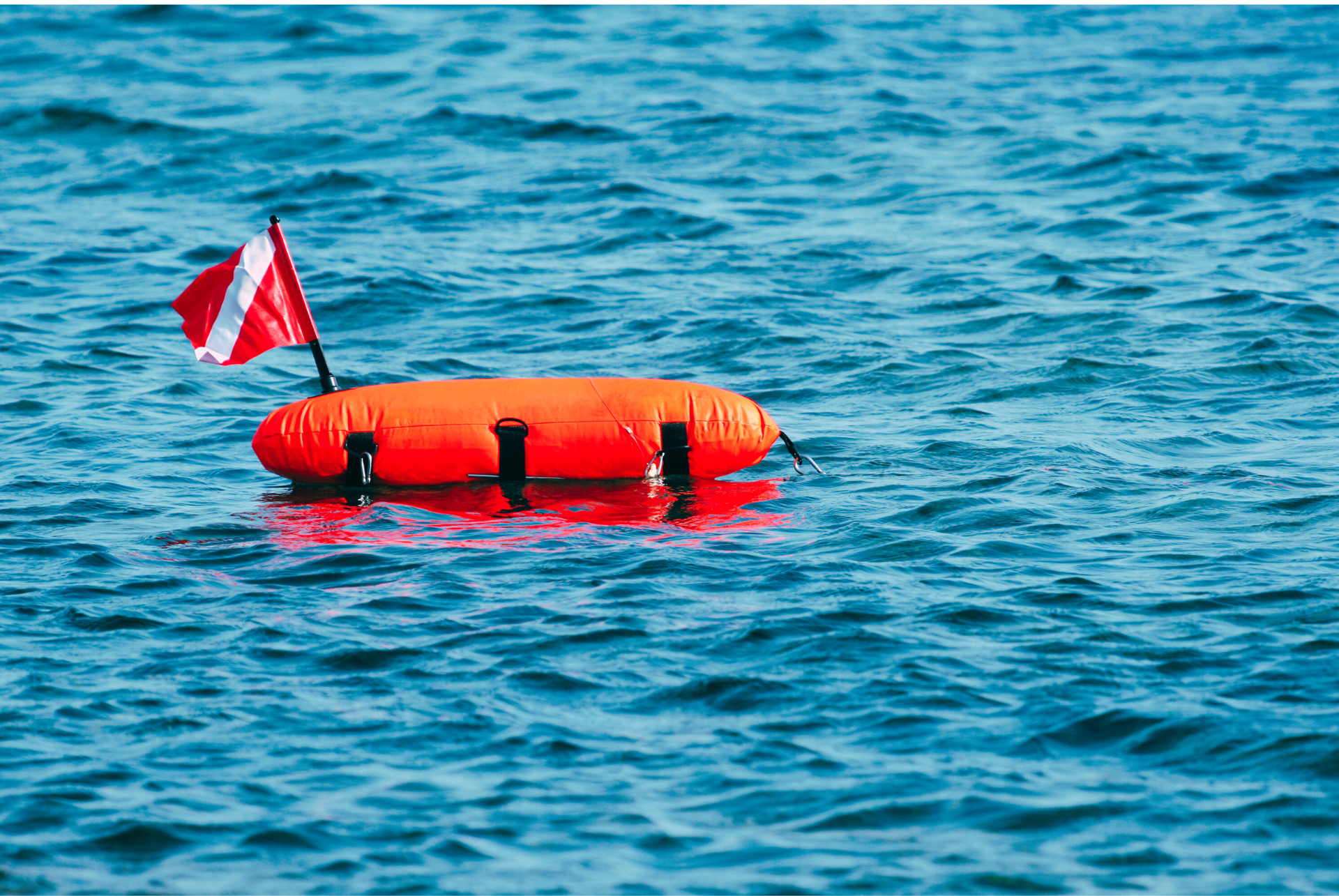 An orange buoy with a flag attached to it is floating on top of a body of water.