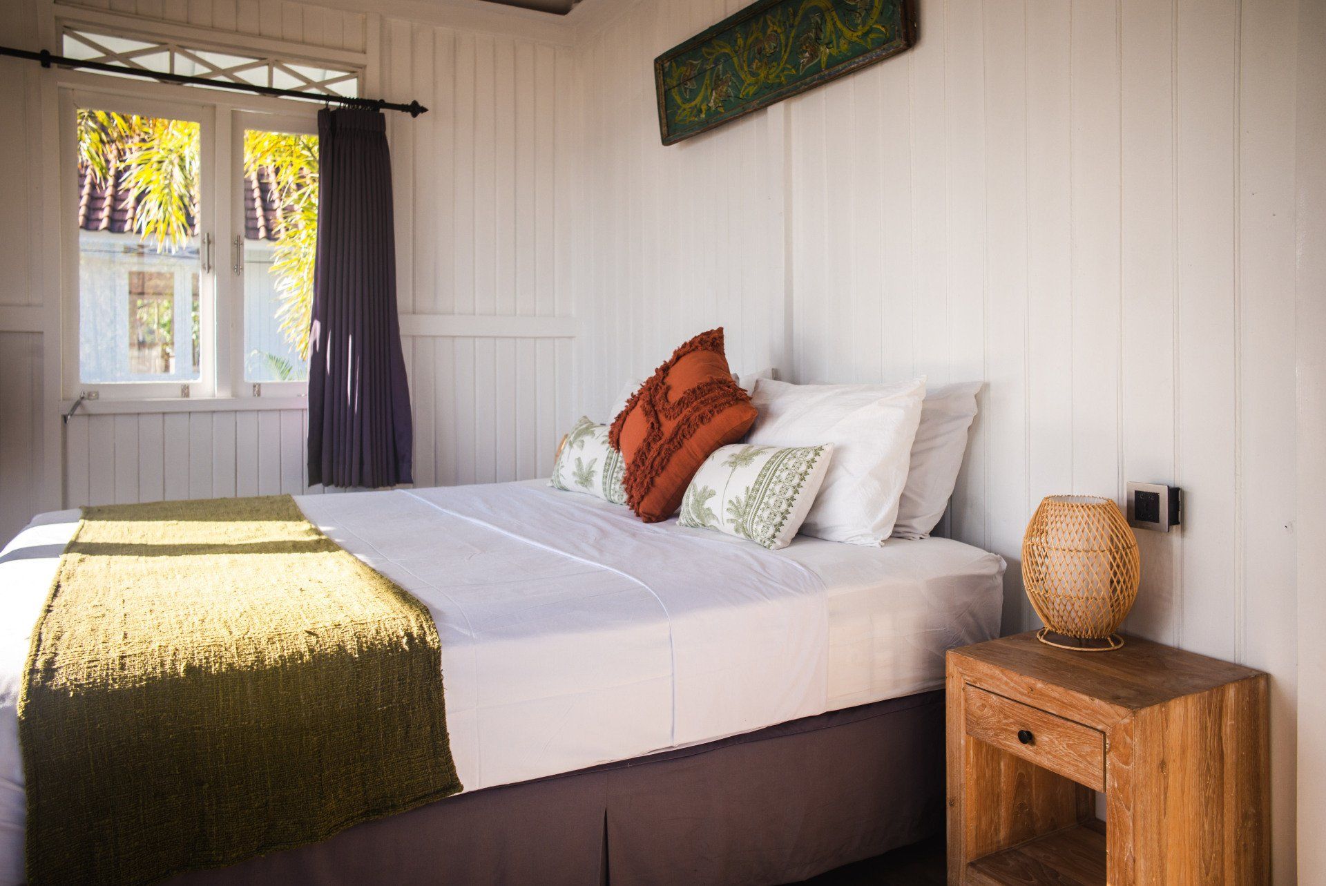 A bedroom with a bed , nightstand , lamp and window.