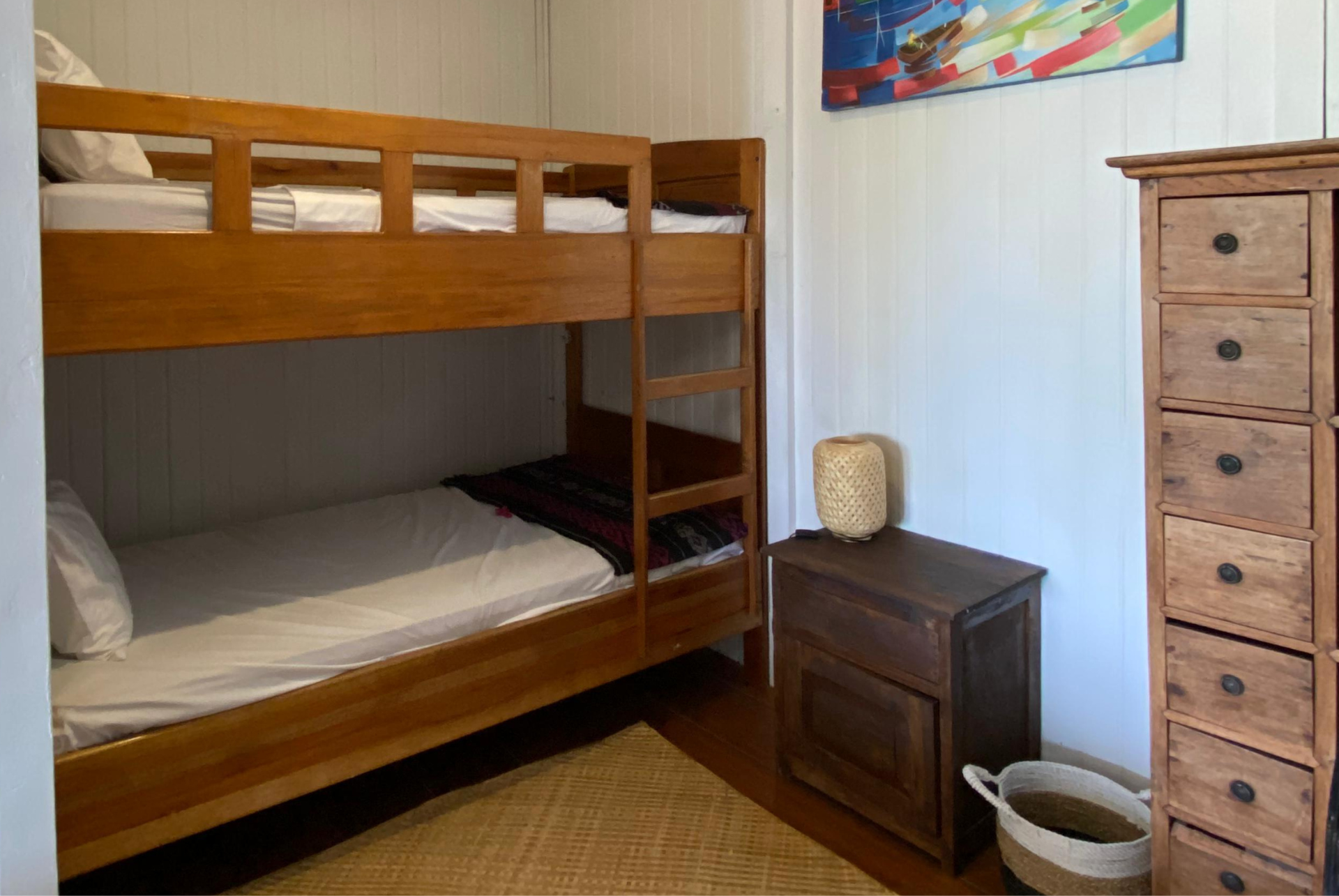 Bunk bed in a room with wooden furniture, a painting, and a woven rug.