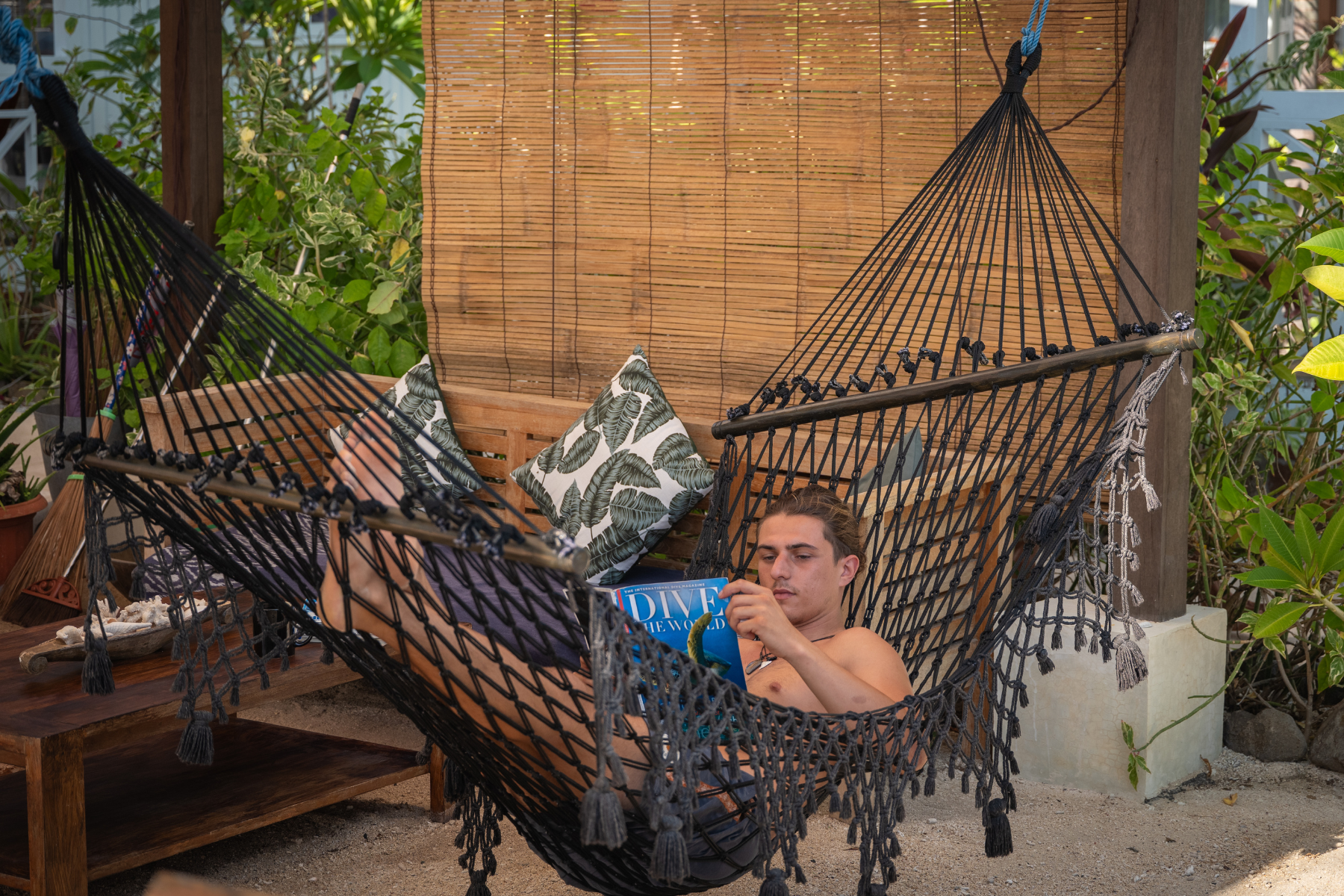 A man is laying in a hammock reading a book.