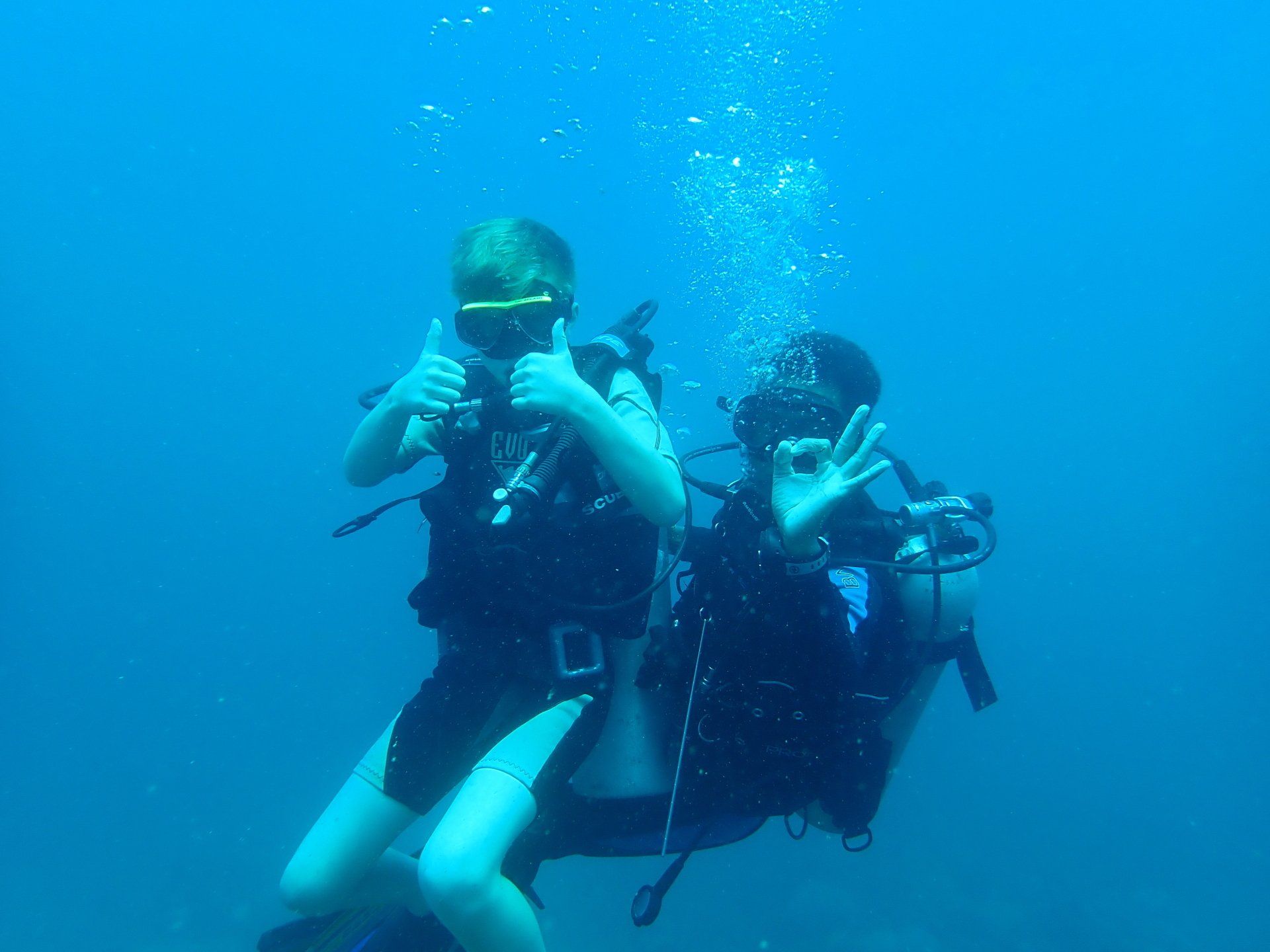 A man and a woman are giving a thumbs up while scuba diving in the ocean.