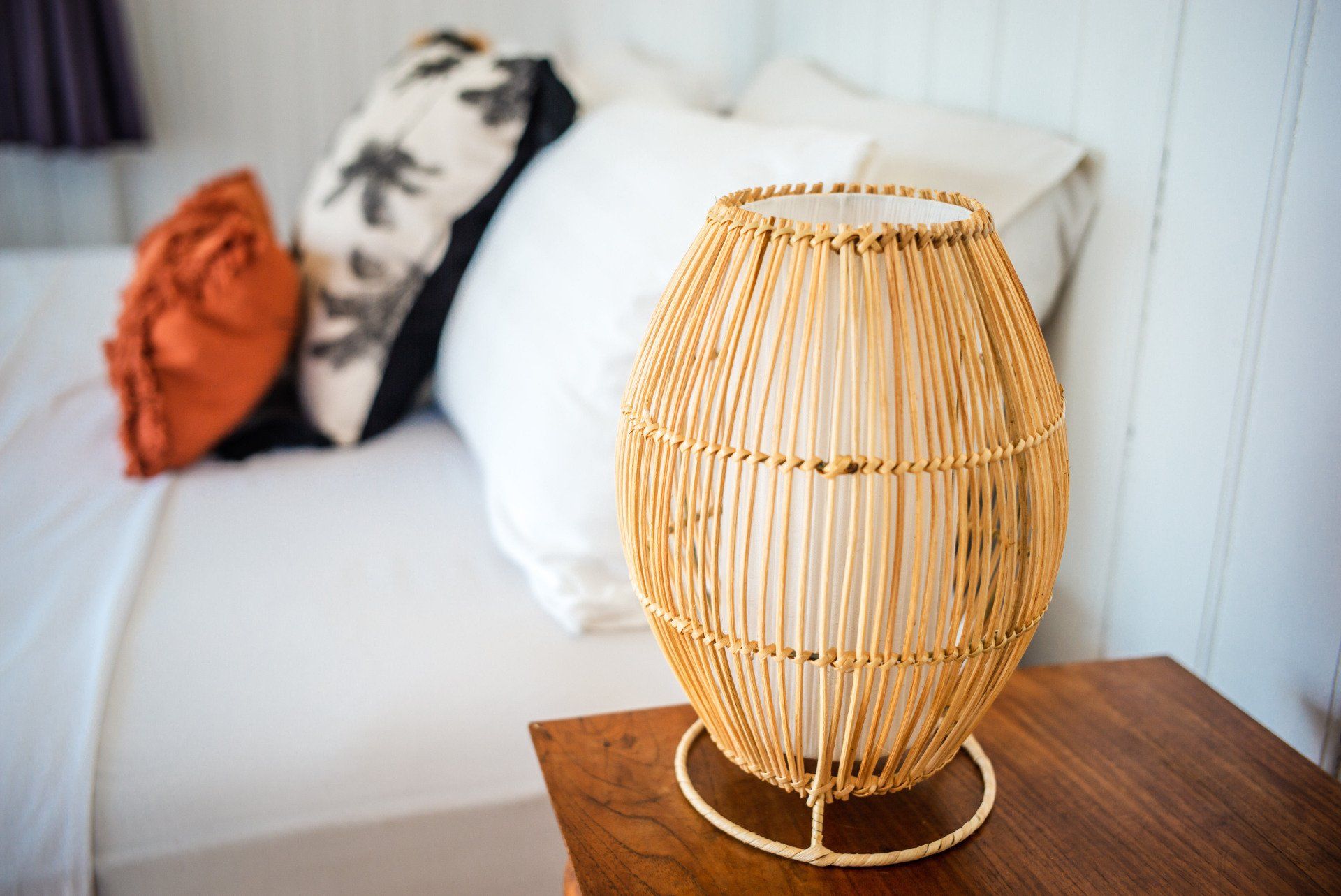 A wicker lamp is sitting on a nightstand in front of a bed.