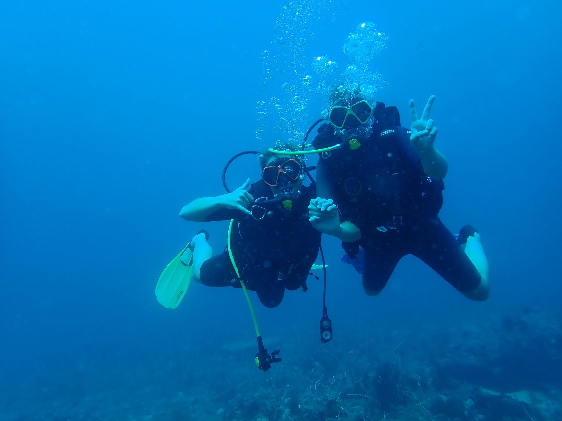 Two scuba divers are giving a peace sign in the ocean.