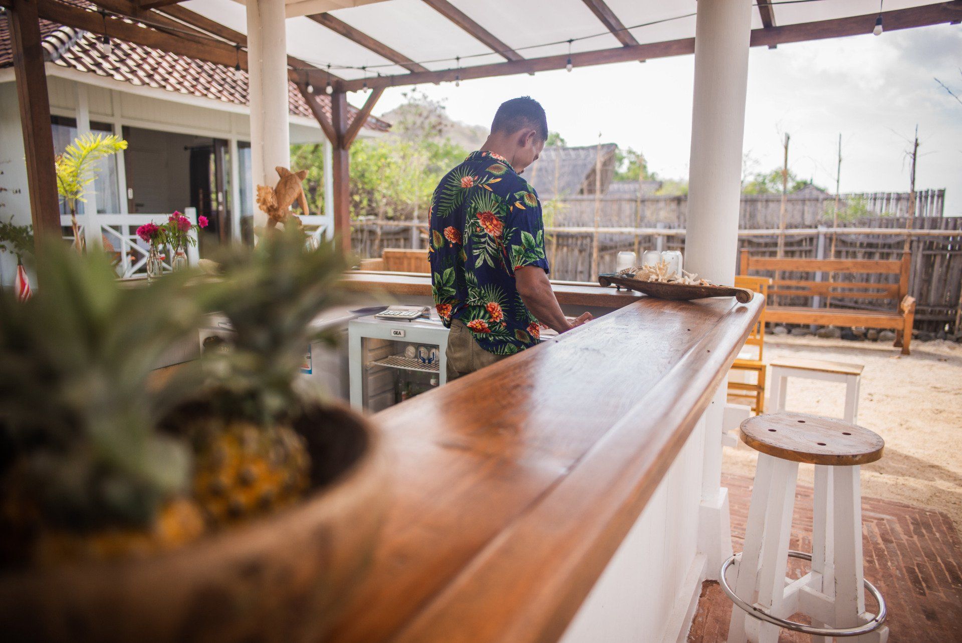 A man in a hawaiian shirt is standing behind a wooden bar.