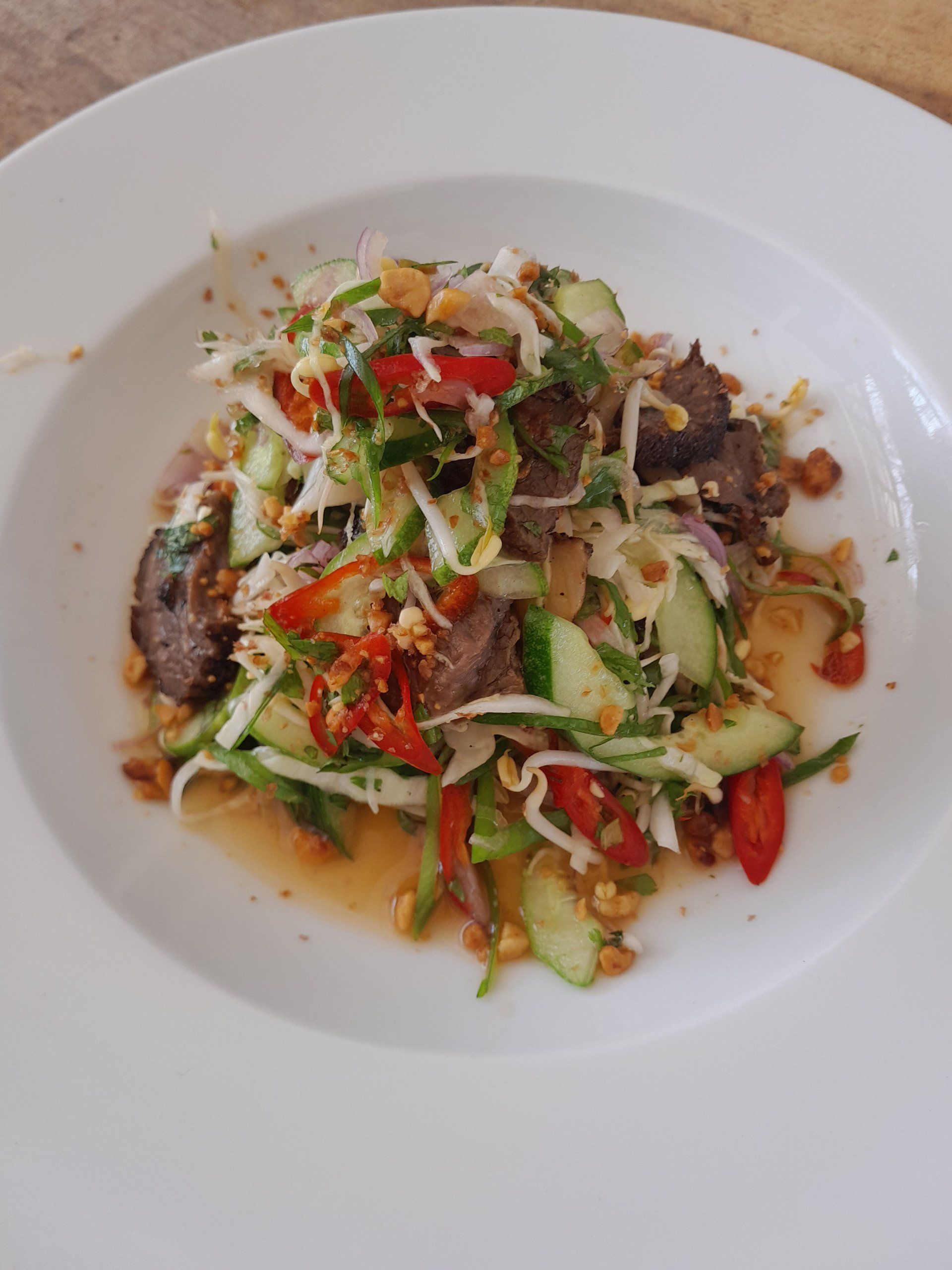 A white plate topped with a salad of vegetables and meat