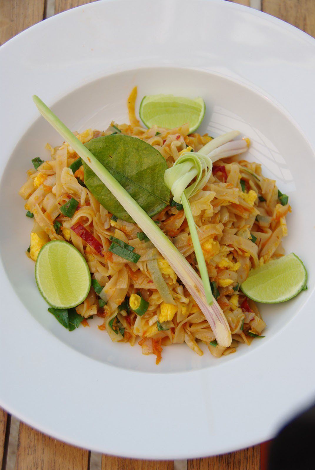 A white plate topped with noodles and vegetables on a wooden table.