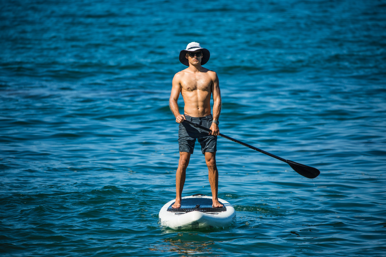 A shirtless man is standing on a paddle board in the ocean.