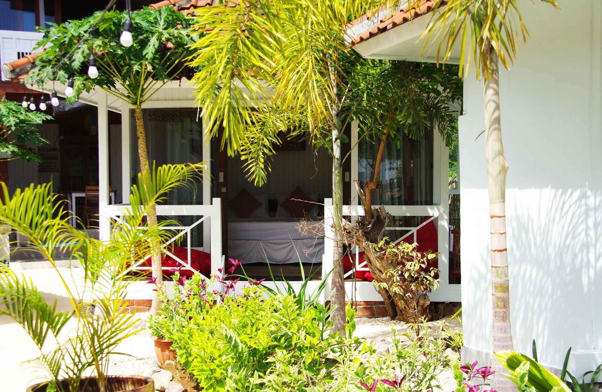 A white house with a porch surrounded by trees and flowers