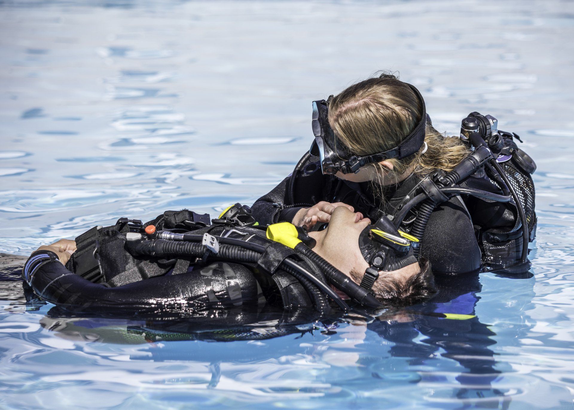 A scuba diver is helping another scuba diver in the water.