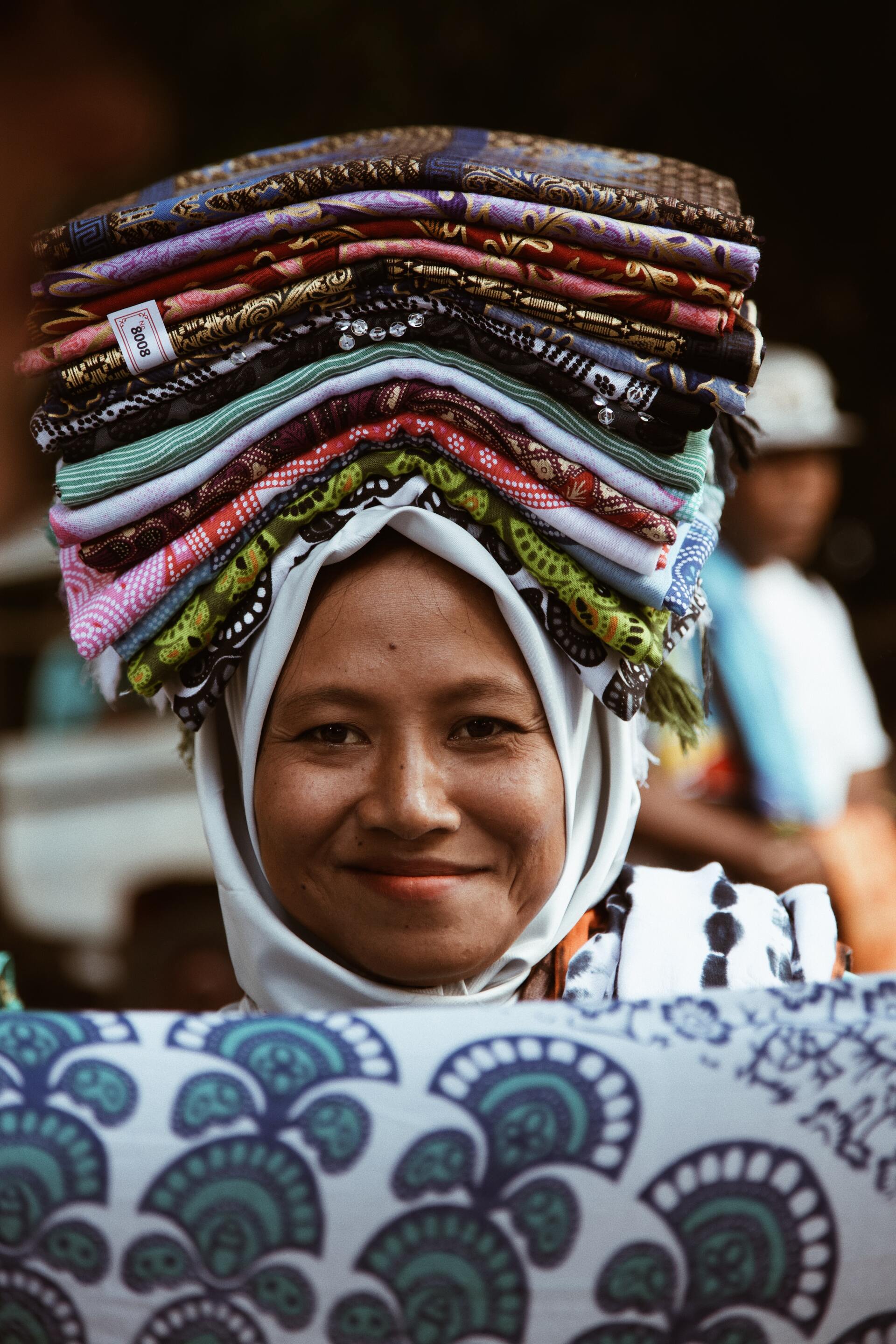 A woman is carrying a stack of clothes on her head.