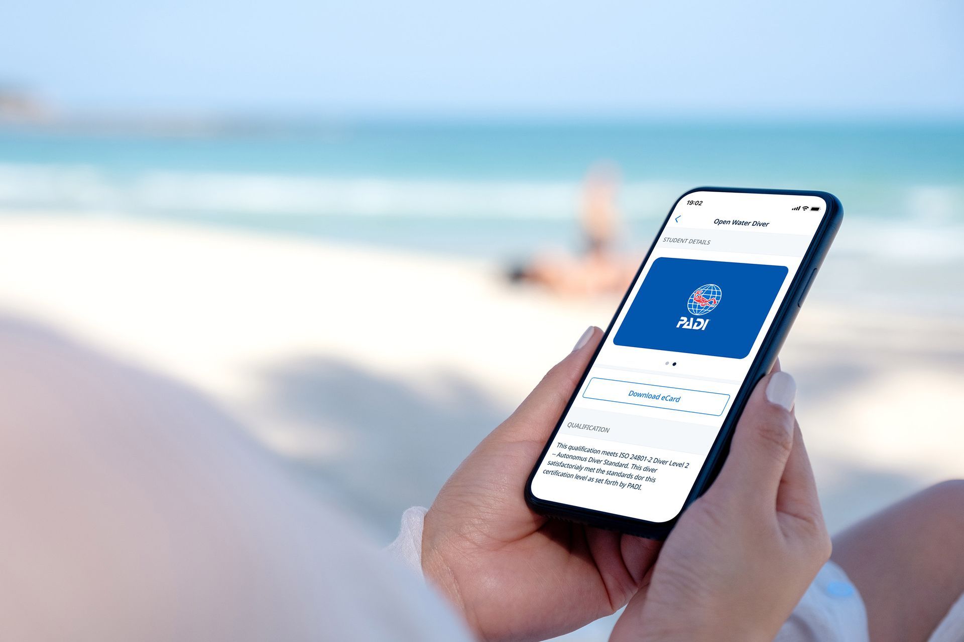 A person is holding a cell phone in their hands on the beach.