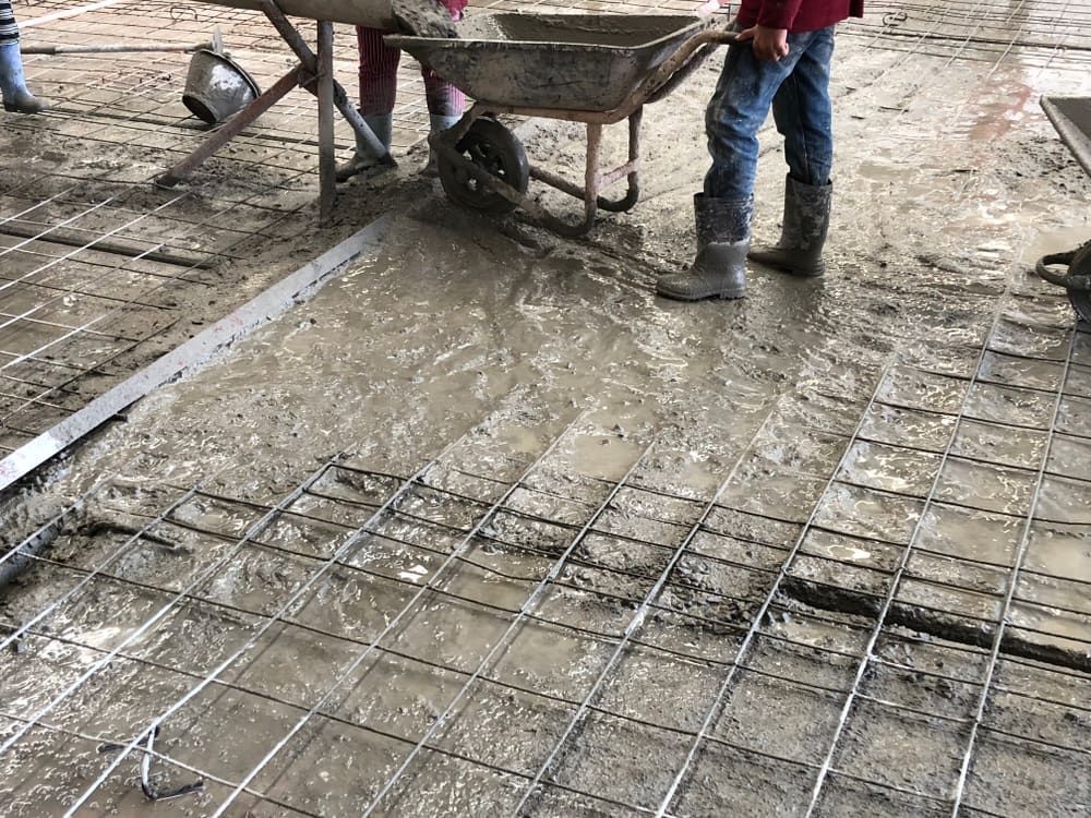 A Man Is Pouring Concrete Into a Wheelbarrow on A Construction Site — Maslin Concrete Pumping in Condobolin, NSW