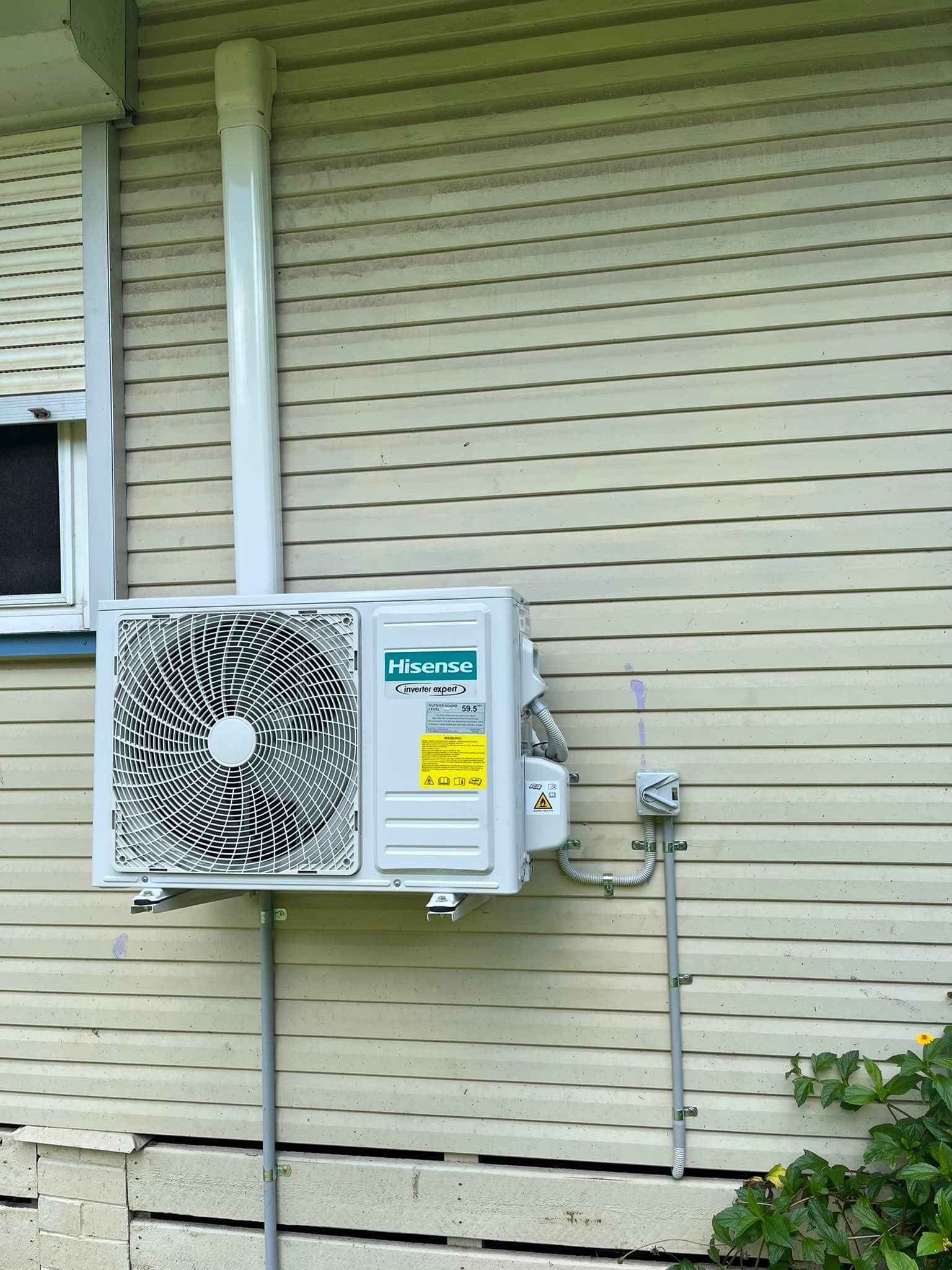 A White Outdoor Air Conditioning Unit Mounted on the Exterior Wall — OHMY Electrical Contractors in Carina, QLD