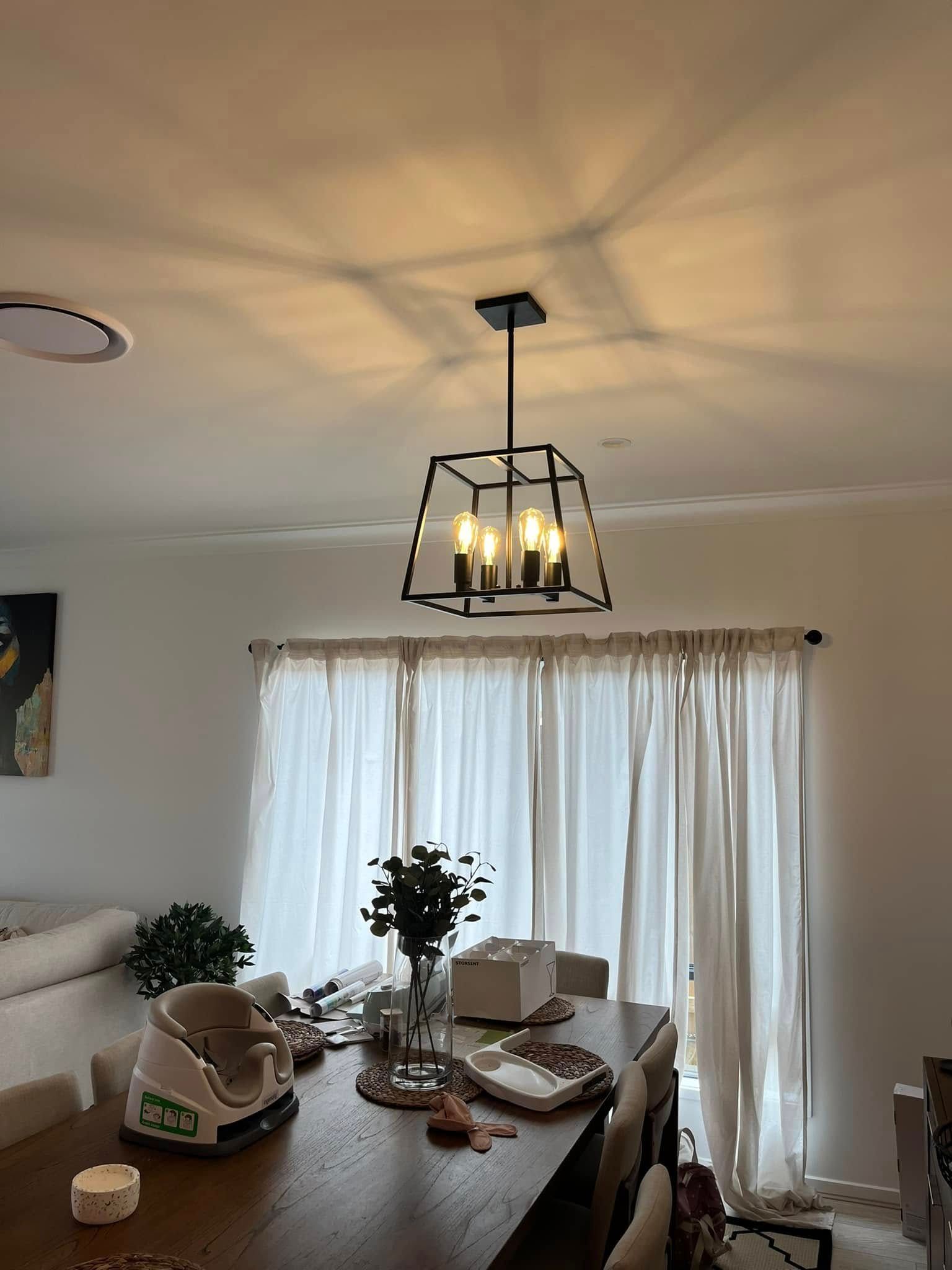 A Four-light Black Metal Lantern Pendant Hangs Above a Wooden Dining Table — OHMY Electrical Contractors in Coorparoo, QLD