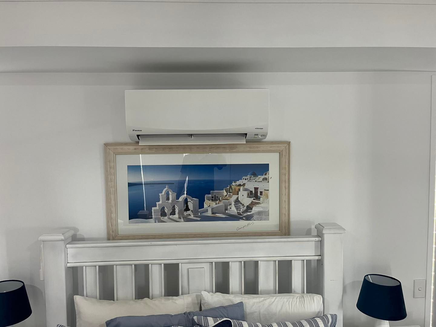 A White Wall-mounted Air Conditioner Sits Above a Framed Landscape Photo — OHMY Electrical Contractors in Coorparoo, QLD