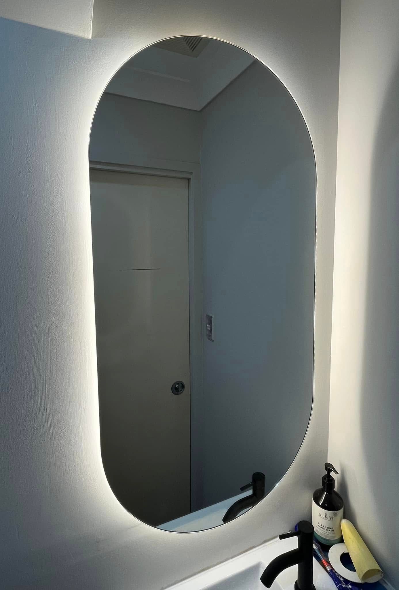 A Backlit Oval Wall Mirror Hangs Above a Bathroom Sink — OHMY Electrical Contractors in Camp Hill, QLD