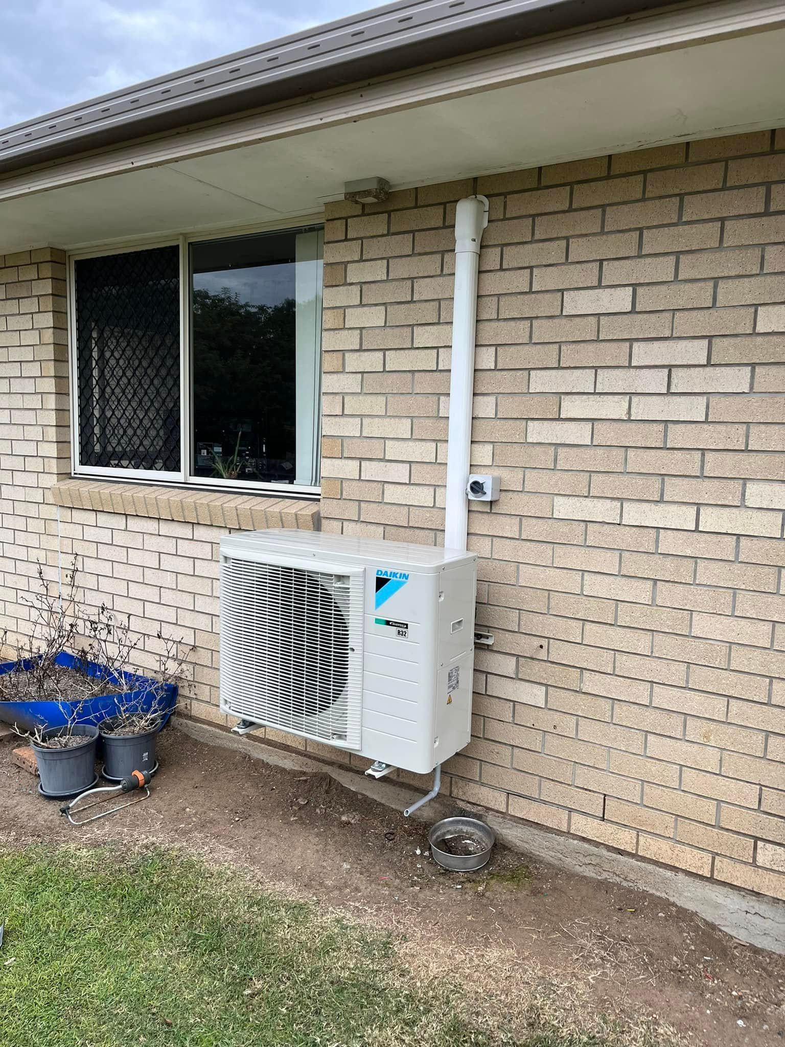 A White Daikin Air Conditioner Outdoor Unit Mounted on a Light Brick Wall — OHMY Electrical Contractors in Mount Gravatt, QLD