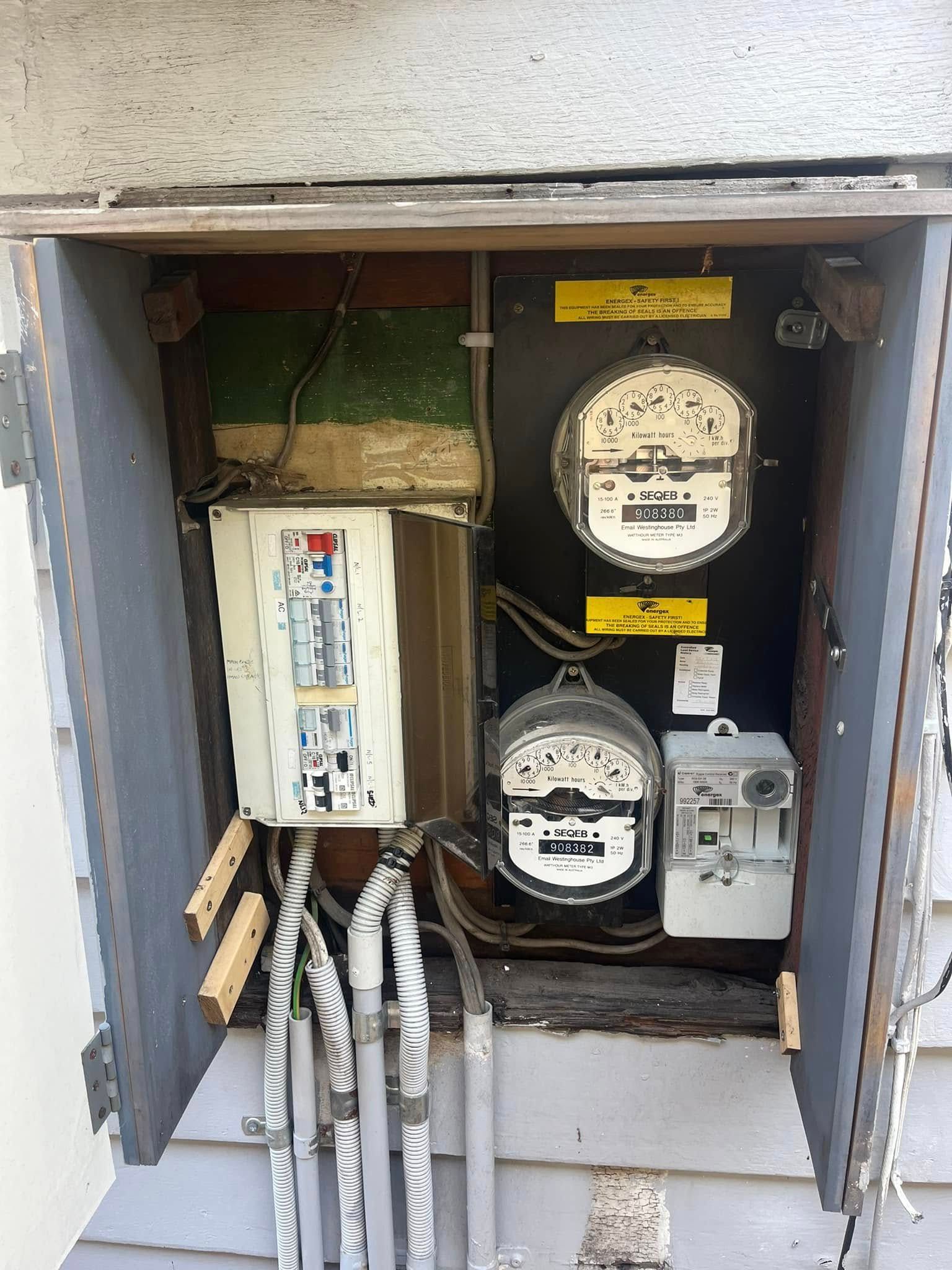 Open electrical meter box with meters, breaker panel, and exposed cables inside a wall recess — OHMY Electrical Contractors in Carina, QLD