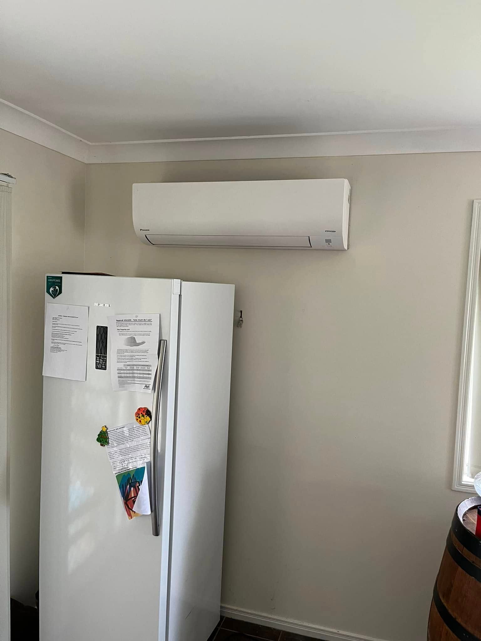 A White Wall-mounted Air Conditioner Positioned Above a White Refrigerator — OHMY Electrical Contractors in Carindale, QLD
