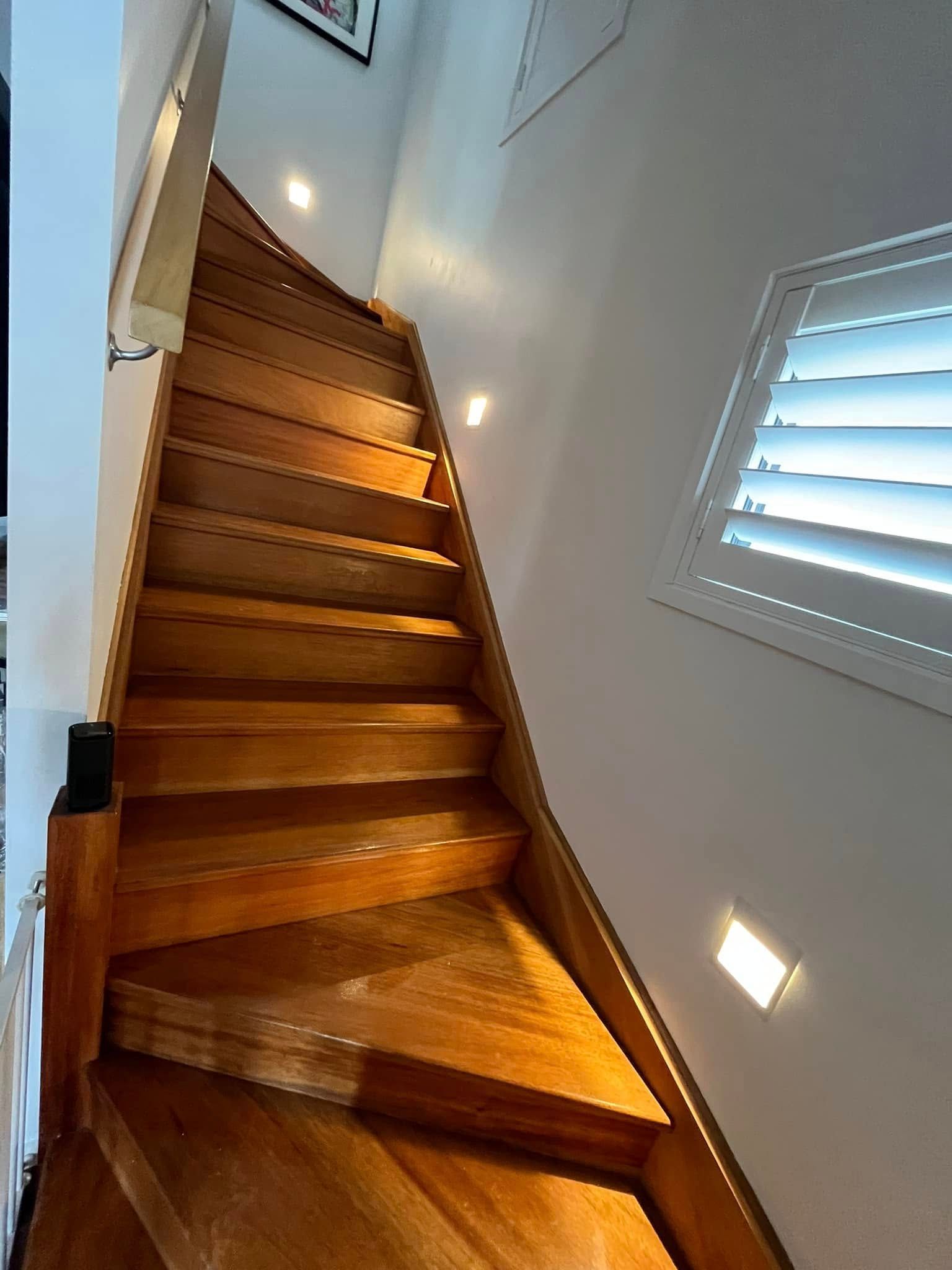 A Wooden Staircase Ascends Between White Walls and a Window With Shutters — OHMY Electrical Contractors in Carina, QLD