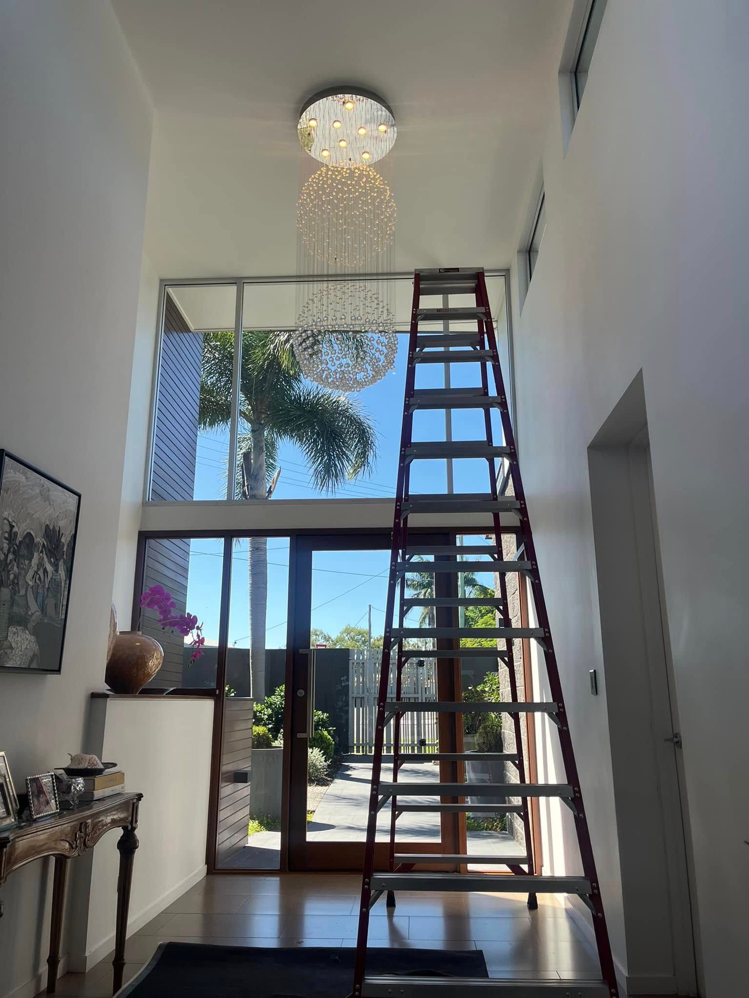 A Ladder Stands in a Bright Foyer, Positioned to Reach a Crystal Chandelier — OHMY Electrical Contractors in Carina, QLD