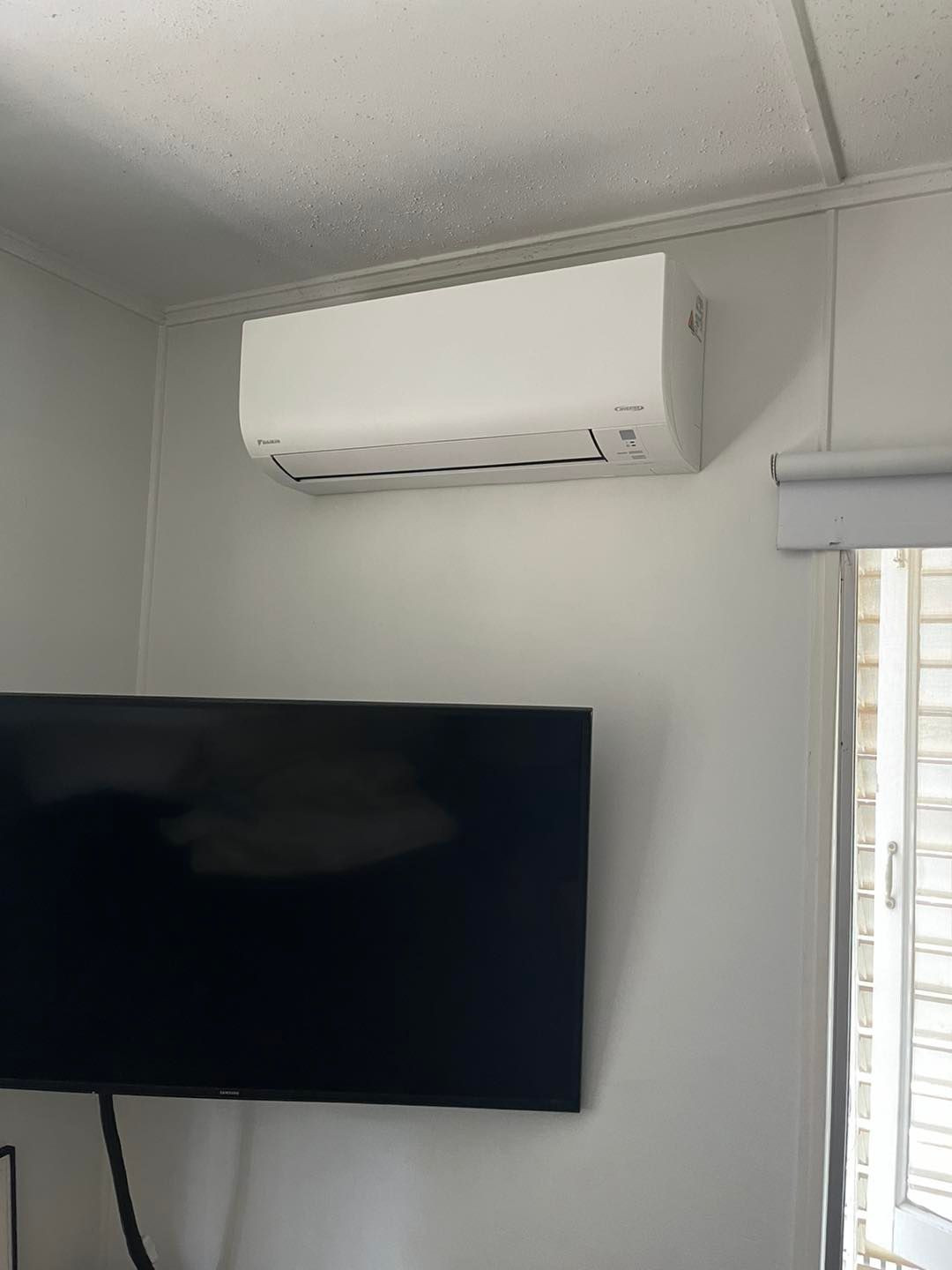 A Wall-mounted White Air Conditioning Unit Installed Above a Black Television — OHMY Electrical Contractors in Carina, QLD