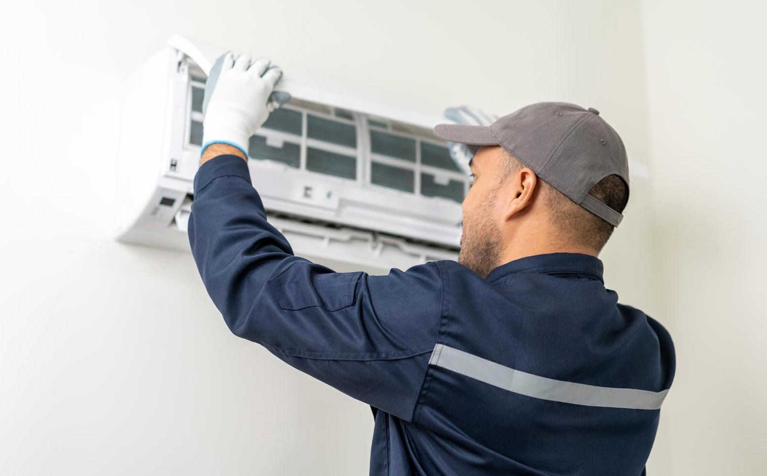 A Technician in a Blue Uniform and Cap Maintains an Air Conditioning Unit — OHMY Electrical Contractors in Carina, QLD