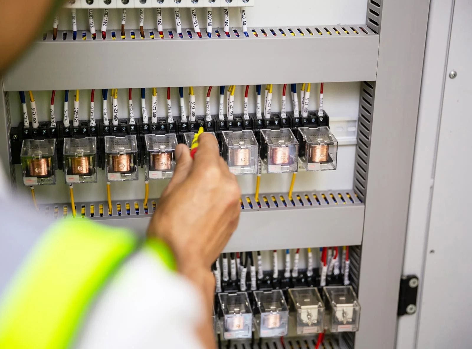 An Electrician in a Vest Checks Electrical Relays in a Control Panel — OHMY Electrical Contractors in Carindale, QLD