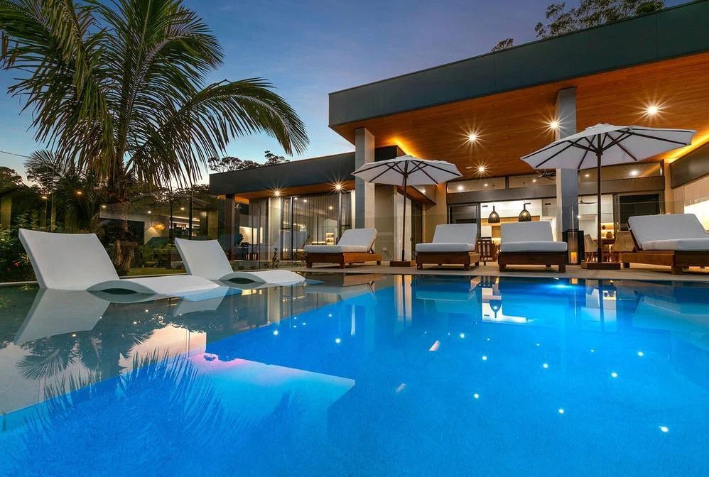 A Luxurious Outdoor Pool With Lounge Chairs at Dusk — OHMY Electrical Contractors in Carina, QLD