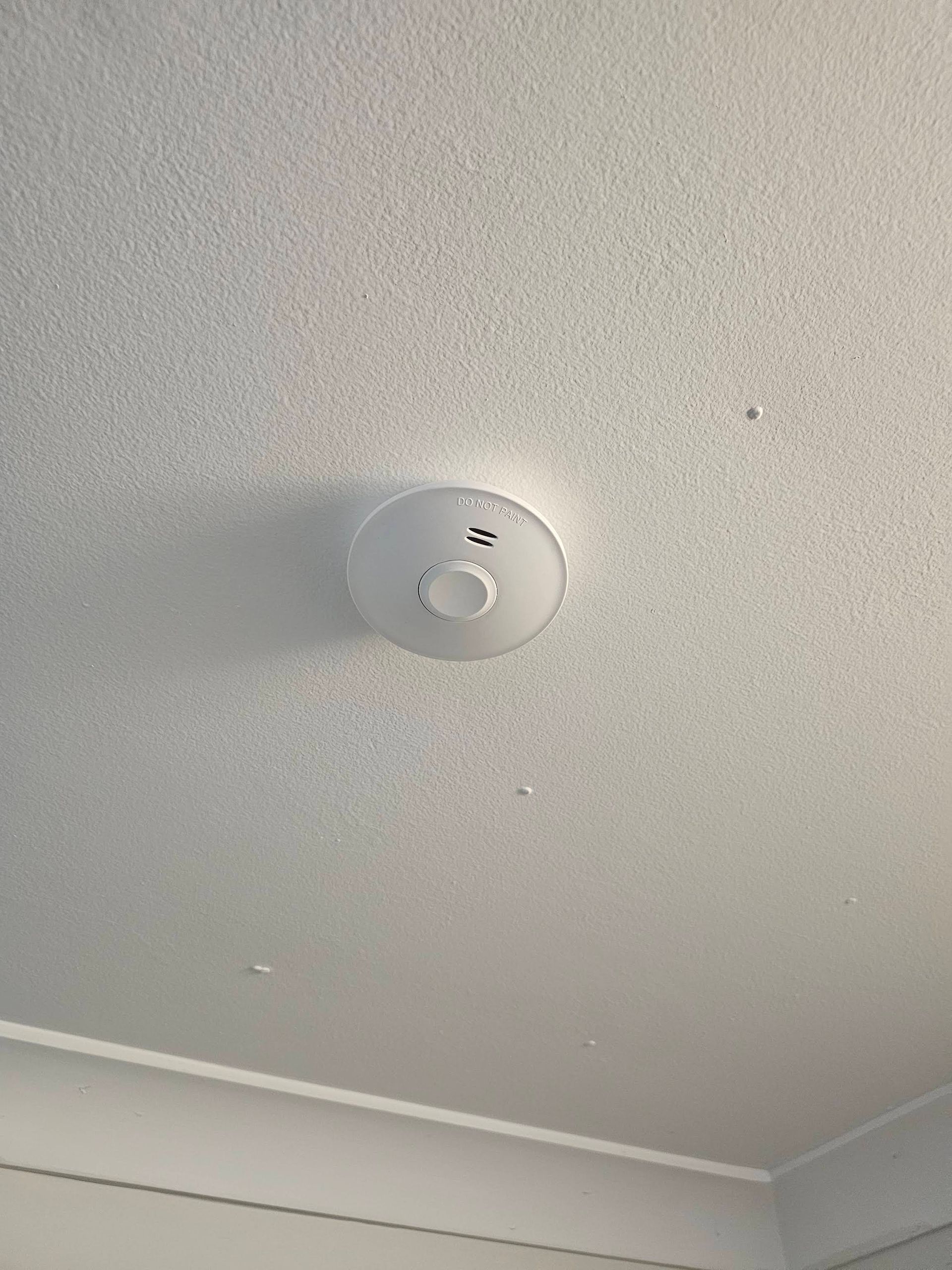 A White Circular Smoke Detector Mounted on a Textured White Ceiling — OHMY Electrical Contractors in Carina, QLD