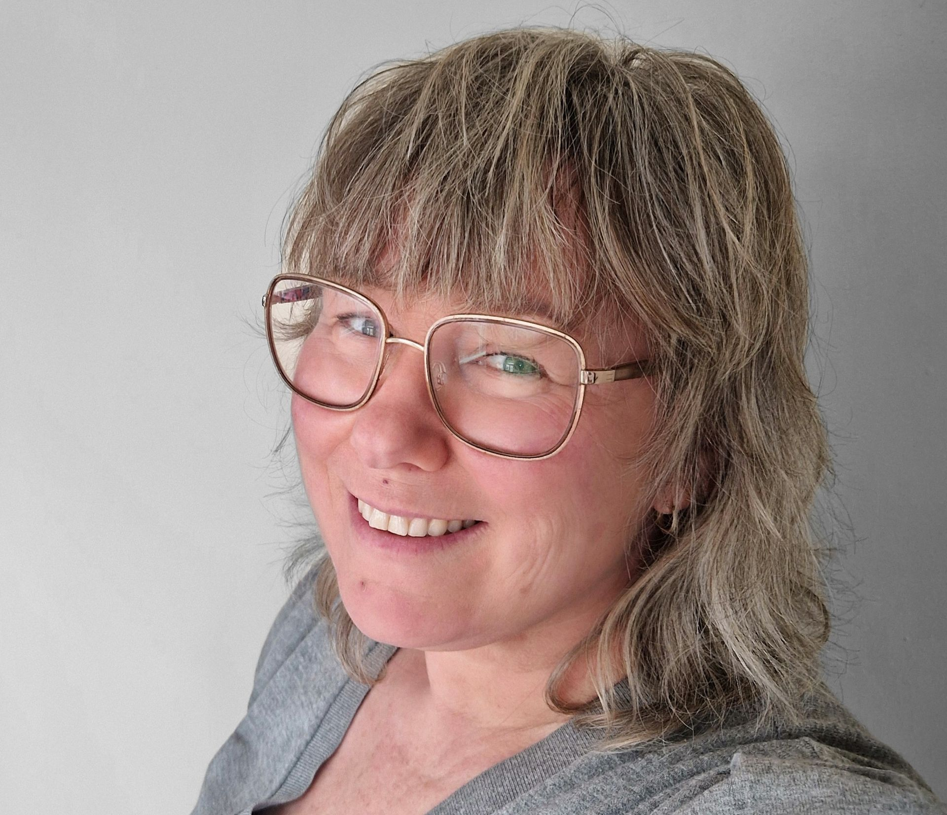 Een lachend persoon met een bril in een witte blouse tegen een effen witte achtergrond.