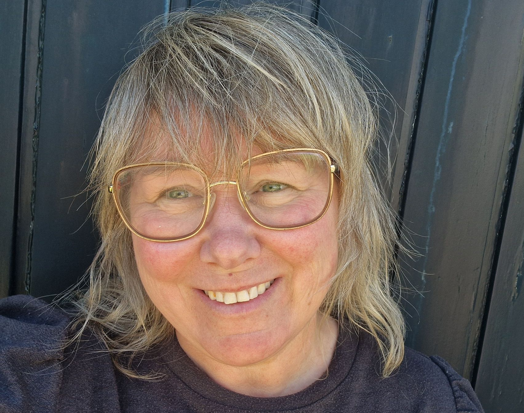 Lachende vrouw met bril en grijs haar, gekleed in een rode top, tegen een witte achtergrond.