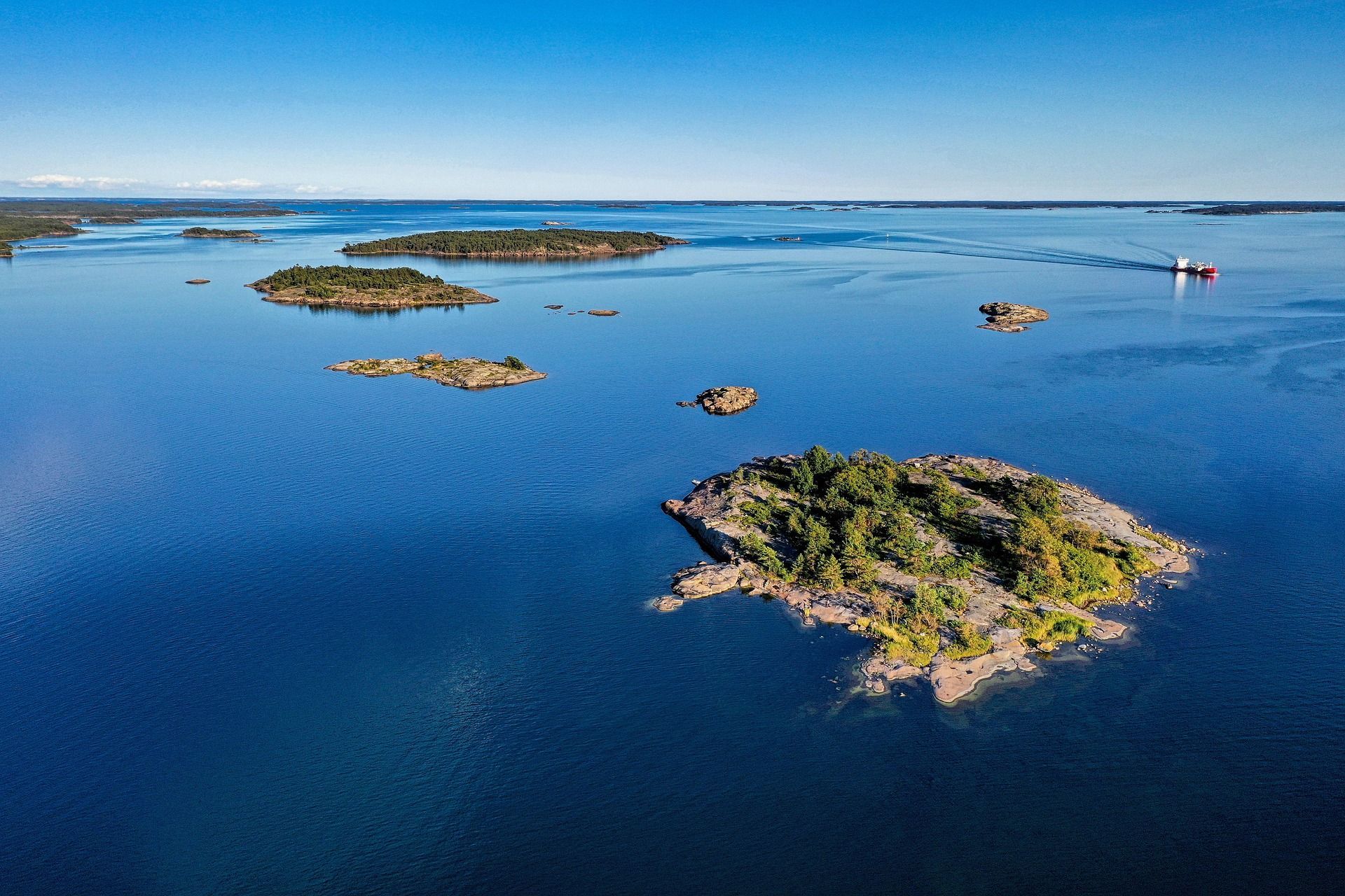Luchtfoto van blauw water met kleine rotsachtige eilandjes en een boot in de verte.