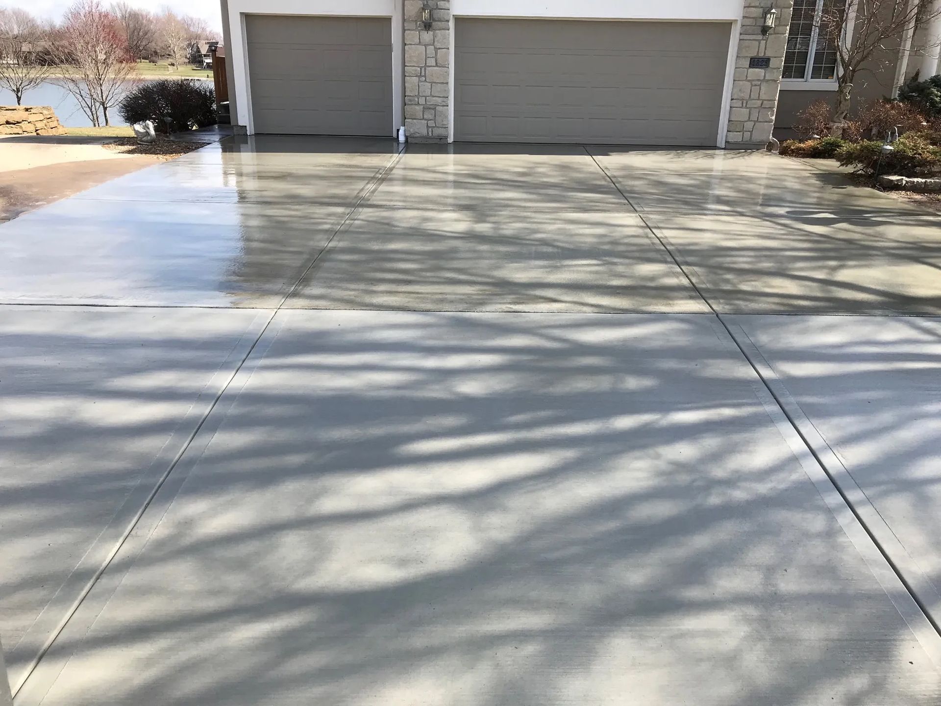Concrete driveway with two garage doors and tree shadows in front of a house