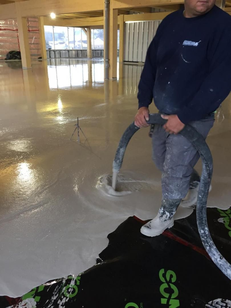 Un homme pompe du liquide dans un sol en béton avec un tuyau.