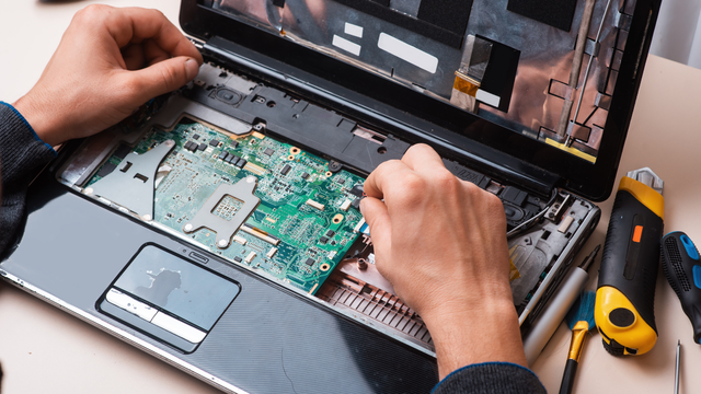 A person is repairing a laptop computer with tools on a table.