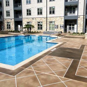 Outdoor apartment pool with blue water, stone deck, and lounge chairs beside a modern building.