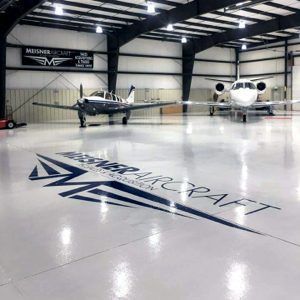 Private hangar with two small aircraft and a large “Mile High Craft” logo on the polished floor