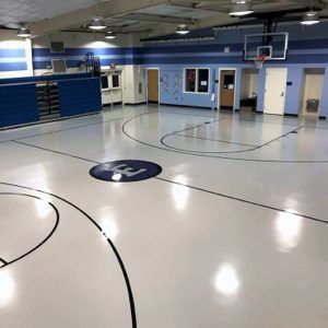 Empty indoor gym with blue walls and a polished floor marked with basketball court lines