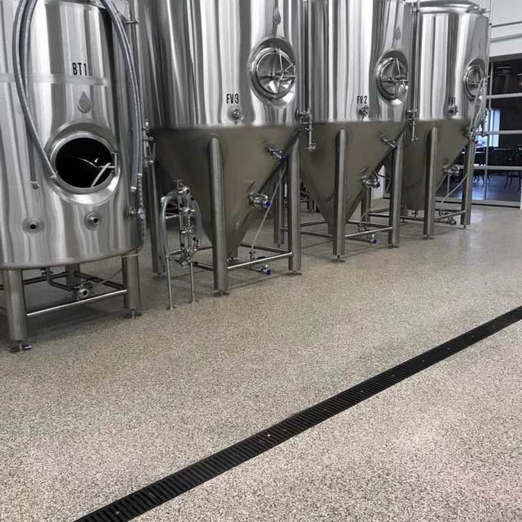 Stainless steel tanks in a clean industrial brewery or food-processing facility with a red floor.