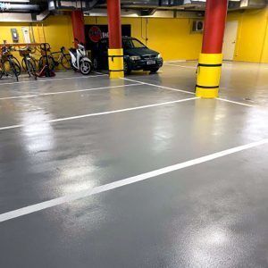 Indoor parking garage with a black car, bicycles, and yellow-red columns on a glossy floor