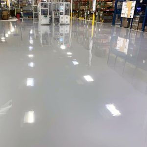 Shiny polished warehouse floor reflecting overhead lights, with industrial equipment and shelving in the background
