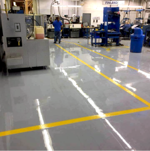 Industrial workshop floor with yellow lines, machinery, and a worker in blue standing near equipment.