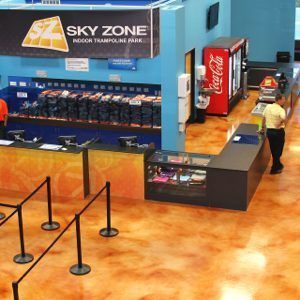 Indoor trampoline park lobby with Sky Zone sign, concession counter, soda machine, and queue stanchions.